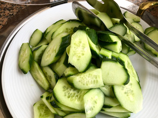 Top view on slices of fresh green cucumbers on a white plate with a metal serving boat. Concept of healthy eating and cafe service.