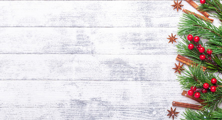 Christmas background with fir tree, spice and red holly on wooden table. Snowfall drawing effect....