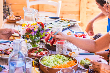 Group of people sharing food and drink. Caucasian peoples enjoying brunch or meal together. Fruits and vegetables on the wooden table. Sunlight outdoor on the terrace