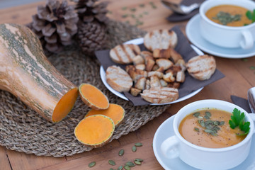 Obraz na płótnie Canvas Healthy eating in autumn and winter time. Wooden table with two bowls of pumpkin cream soup. In the middle of the table bread croutons.