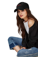 Full length shot of a dark-haired girl, sitting on a floor and wearing black baseball cap with...