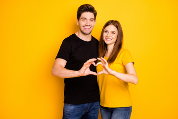 Photo of cheerful charming cute sweet pretty nice couple shaping heart with their fingers symbolizing love in black t-shirt jeans denim isolated yellow vivid color background