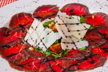Beef carpaccio on a white plate with rucola and Parmesan