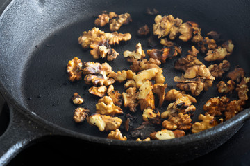 Walnuts cooking in a cast iron frying pan on a ceramic hob stove