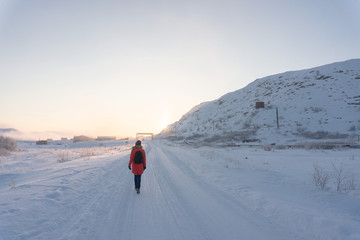 a lonely girl in a bright jacket walks along a white snowy road through the tundra beyond the Arctic Circle on a frosty clear day