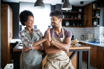 Young happy couple in aprons giving high five in kitchen