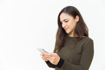 Focused serious cellphone user texting message. Young woman in casual with mobile phone standing isolated over white background. Wireless technology concept