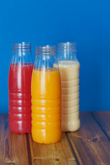 three bottles of milkshake stand on a wooden table on a blue background
