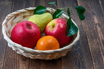 fresh fruits in a straw basket on a dark wooden background close up