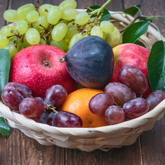 red and white grapes and fresh fruits in a straw basket on a dark wooden background