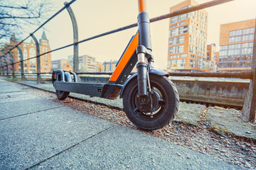 Orange colored e-scooter front perspective view parked outdoor on pavement of urban city scene
