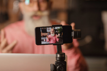 Bearded senior blogger recording video at home.