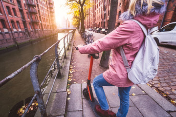 Back view of adult woman tourist with backpack discover Hamburg city on e-scooter. Most famous historic Speicherstadt warehouse district, Germany, Europe