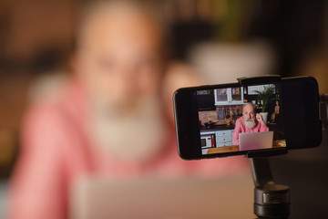 Bearded senior blogger recording video at home.