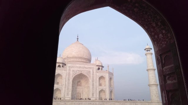 Taj Mahal the famous UNESCO site walking through framing marble arch with the local people and tourist at distance. Agra, India.