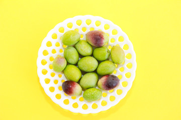 natural green and brown olives in a decorative plate on a yellow background