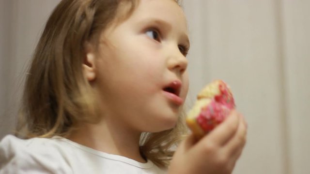 Child mouth bites rose donut. Closeup baby girl eating doughnut with glase. Delicious, sweet, sweettooth