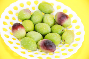 natural green and brown olives in a decorative plate on a yellow background