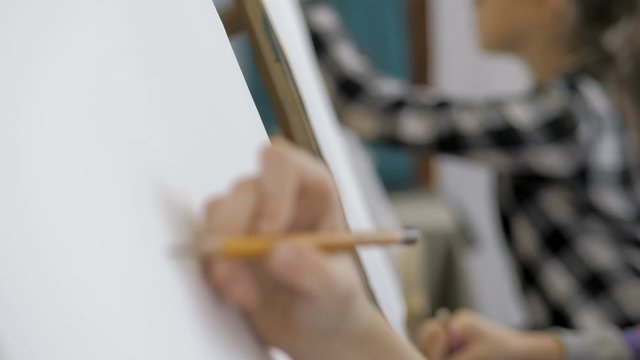 Closeup of kid's hand paints a picture with a pencil on canvas