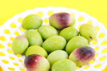 natural green and brown olives in a decorative plate on a yellow background