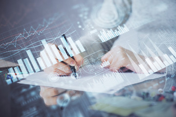 Hand taking notes in notepad. Forex chart holograms in front. Concept of research. Multi exposure