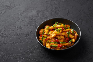 Baby Corn Manchurian dry looks like Schezwan Baby Corn in black bowl at dark slate background. Baby Corn Manchurian - is indo chinese cuisine dish with deep fried corn, bell peppers, sauce and onion.