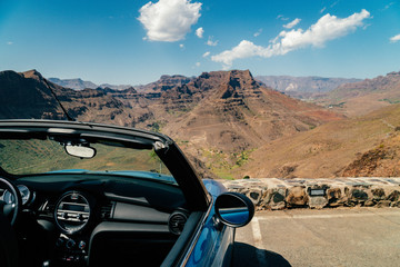 View of the canyon from Degollada de La Yegua viewpoint on San Bartolome de Tirajana, Gran Canaria island in tropical Canary island, Spain in Atlantic ocean.  Parked convertible blue car in foreground - obrazy, fototapety, plakaty