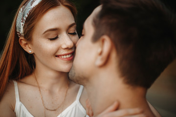 Close up portrait of a beautiful young caucasian woman with red hair and freckles smiling with closed eyes before kissing with her boyfriend outdoor in the park