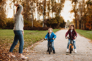 Fototapeta premium Mother giving the start while her son and daughter laughing waiting to go ahead on the bycoke. Mother and her kids playing outdoor.