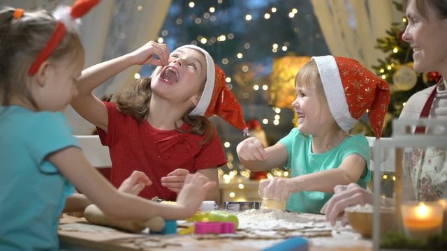 Woman and three little girls baking Christmas cookies. Children with their mom making gingerbread for family dinner on Christmas eve. Kids laughing and fooling around and eating sweet dough.