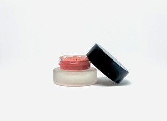 Open, small container of soft pink cheek blush makeup on a white background.