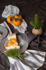 persimmon cheesecake on a dark background. Pieces of cake decorated with persimmons and Christmas tree branches.