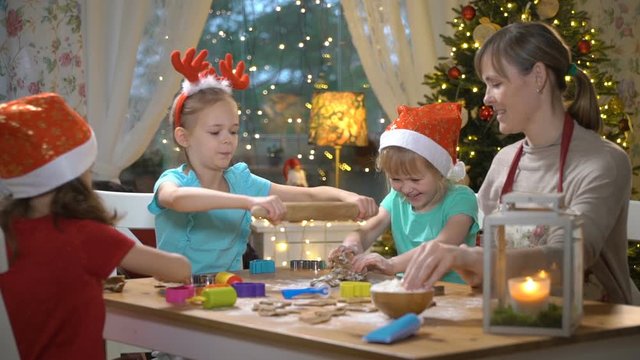 Woman and little girls baking Christmas cookies. Children with their mom making gingerbread for family dinner on Christmas eve in dining room with christmas tree and candles.