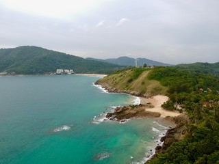 Wind turbine  Panorama drone aerial view electricity windmill overlooking Naiharn beach phuket Thailand turquoise blue waters white golden sandy beach lush green mountains 