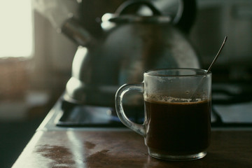  Kitchen. A metal kettle boils on the stove. A cup of coffee. Window. Brown set.
