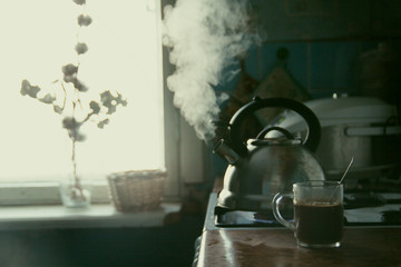  Kitchen. A metal kettle boils on the stove. A cup of coffee. Window. Brown set.