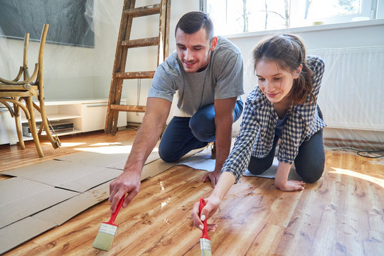Young couple together paint the plank floor