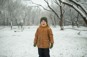 cheerful kid in a yellow down jacket and military hat enjoys snow in winter