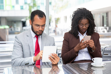 Confident businesspeople using modern devices. Focused African American colleagues holding smartphone and tablet. Technology concept