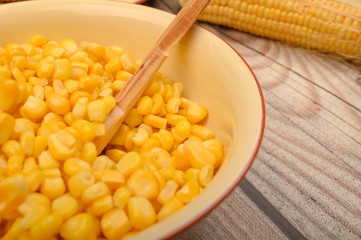 Grains of sweet corn in a plate with a wooden spoon and ears of corn on the table. Healthy diet. Fitness diet. For a sweet treat. Close up.