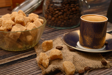 Pieces of brown sugar in a sugar bowl, a Cup of coffee, coffee beans on a wooden background. Close up.