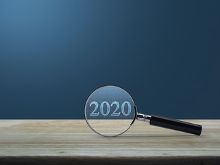 Magnifying glass with 2020 text and financial graph on wooden table over light blue gradient background, Business happy new year research concept