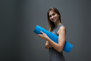 Young sportswoman with blue rug in hands on background of gray wall