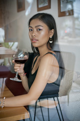 Asian girl in a cafe. Beautiful Balinese women with glass of wine with window reflection