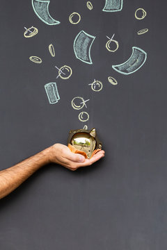 Concept of saving money with a golden piggy bank held in a hand in front of a blackboard with hand drawn coins and banknotes