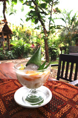 glass of coconut milk indonesian traditional drink consist of various of fruits on table in garden