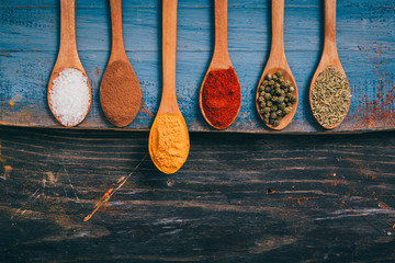 flat lay of colorful spices in spoons on wooden table with copy space. tumeric stands out - obrazy, fototapety, plakaty