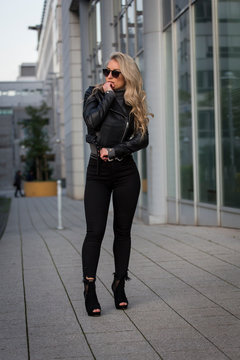 Frau, jung, blond ,sch&ouml;n, modisch, modebewusst und schlank geht im Herbst mit Lederjacke und engen Jeans und Pumps Hackenschuhe durch die Stadt