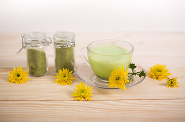 Cup of matcha green tea latte on wooden background.  Still life matcha tea, powdrer and yellow flowers.