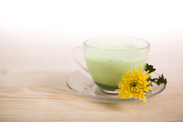 Obraz na płótnie Canvas Cup of matcha green tea latte on wooden background. Still life matcha tea, powdrer and yellow flowers.